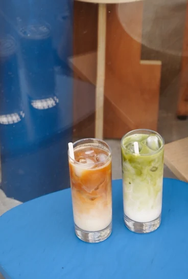 Un café glacé au lait et un matcha glacé sur une table bleue