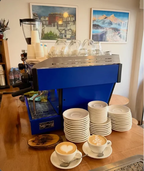 La machine à espresso bleue, deux cappuccinos et, au mur, des tableaux du Potala et de l’Himalaya