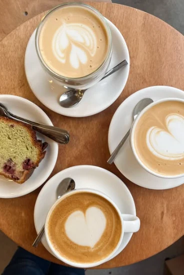 Trois cafés au cœur et une part de cake pistache-framboise sur une table en bois